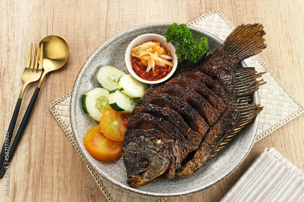 Gurame Bakar Madu, Grilled Gourami with honey and soy sauce. Served with sambal (chilli sauce), cucumber and tomatoes in white plate.
Gurame Bakar Madu, Grilled Gourami with honey and soy sauce. Served with sambal (chilli sauce), cucumber and tomatoes in white plate.