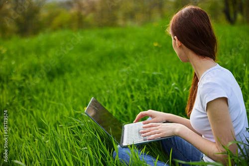 Young beautiful woman using laptop on meadow