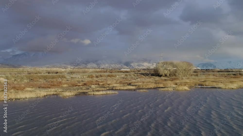 aerial orbit dramatic golden hour over a large lake in utah usa with dark clouds over snow covered mountains and a geothermal smoke stack. aerial orbit dramatic golden hour over a large lake in utah usa with dark clouds over snow covered mountains and a geothermal smoke stack.