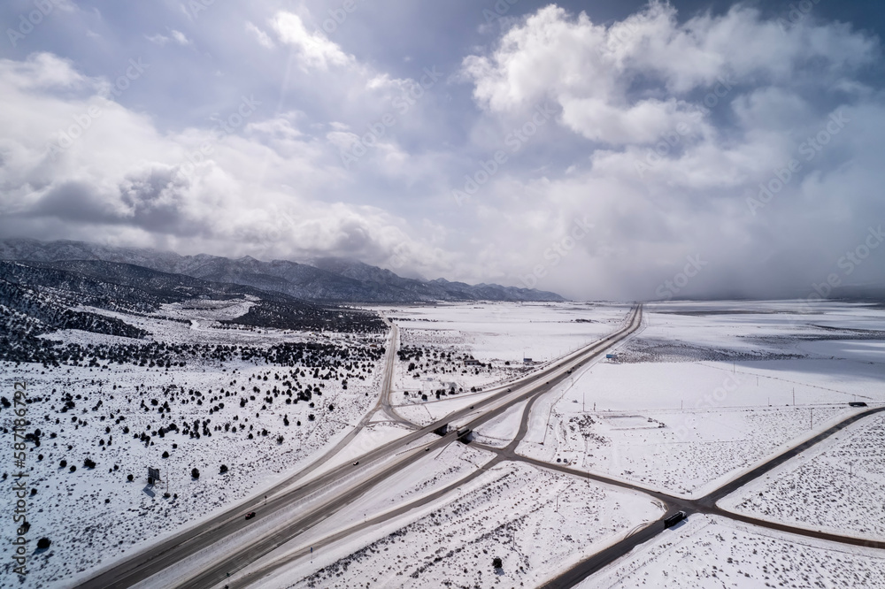 Aerial view of highway in California after snow storm with traffic. Trucks and cars are going on interstate along mountains and deserts.