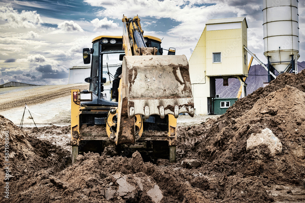 A universal excavator is working on a construction site against a cloudy sky. Earthworks at a construction site. Modern earthmoving equipment. The contractor is doing construction work. A universal excavator is working on a construction site against a cloudy sky. Earthworks at a construction site. Modern earthmoving equipment. The contractor is doing construction work.