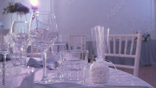 Empty glasses, napkins and gift wrapped craft marshmallows stand on table in beautiful blue room. Nearby are chiavari chairs, spotlight flickers beautifully on counter next to flower arrangement. photo