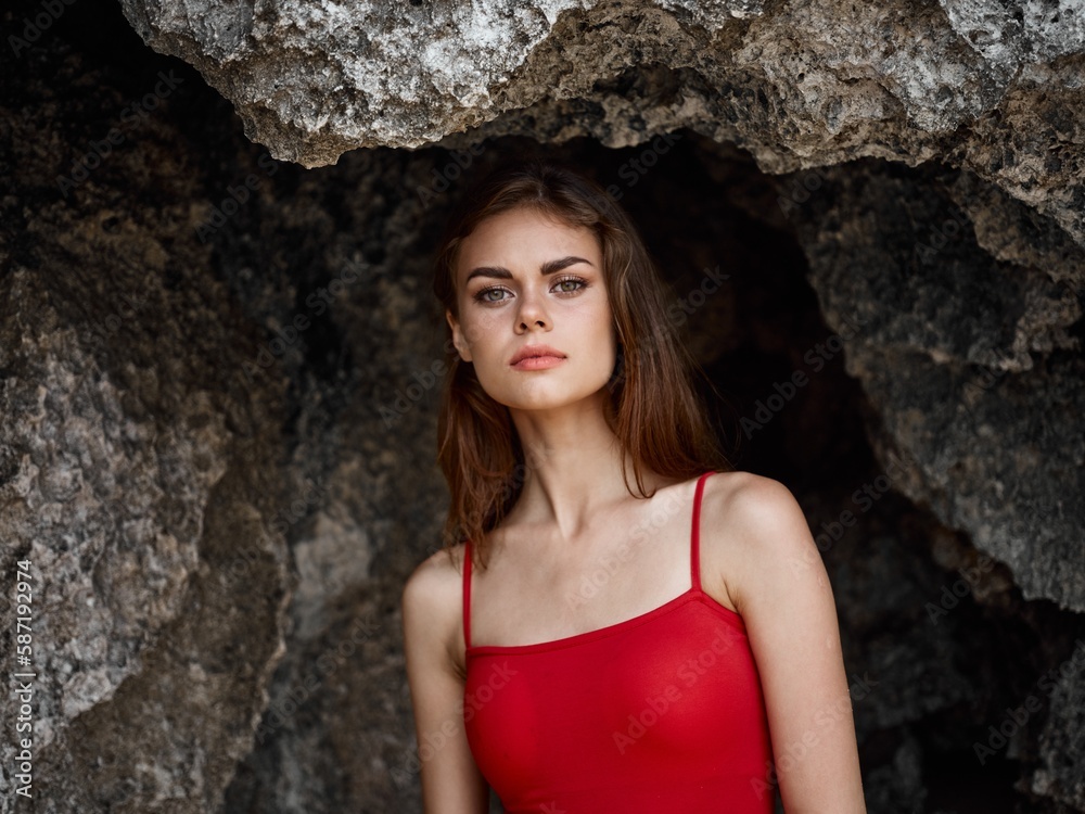 Portrait of a woman in a red swimsuit against the rocks by the ocean, tanned skin from the sun, the concept of protecting skin from the sun and body health Portrait of a woman in a red swimsuit against the rocks by the ocean, tanned skin from the sun, the concept of protecting skin from the sun and body health