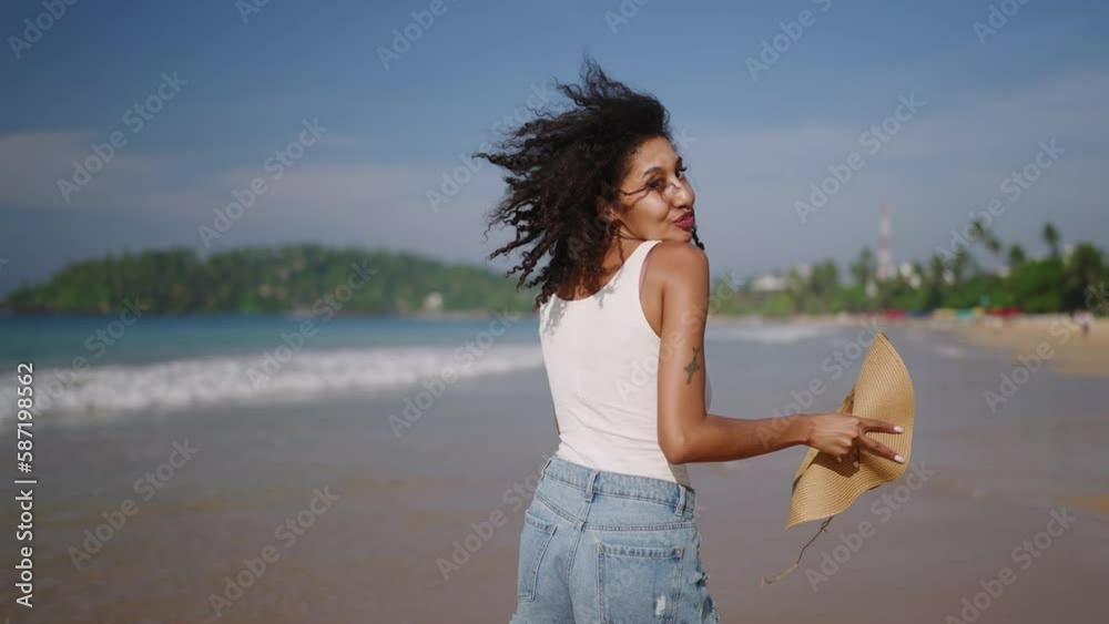 Multiethnic black woman runs on ocean beach on tropical vacation at exotic island. African american female turns, flirts running on sea shore with straw hat. Bipoc has fun on travel tour. Follow me. Multiethnic black woman runs on ocean beach on tropical vacation at exotic island. African american female turns, flirts running on sea shore with straw hat. Bipoc has fun on travel tour. Follow me.