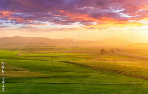 beautiful green valley with green fields with green spring grass with nive hills and mountains and scrnic colorful cloudy sunset on background of landscape