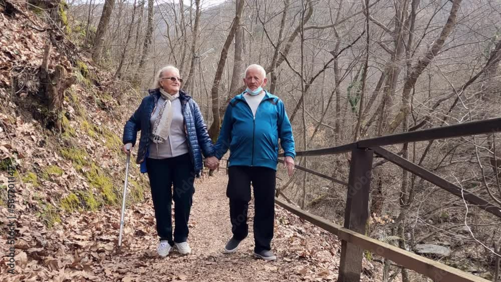 Romantic elderly couple walking together through the forest while using crutches holding hands, slow motion Romantic elderly couple walking together through the forest while using crutches holding hands, slow motion
