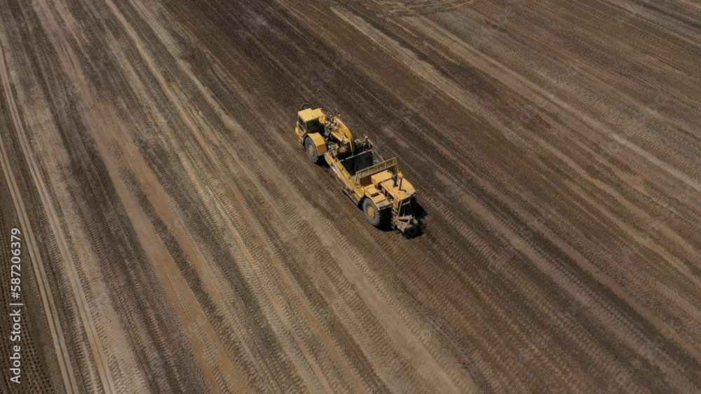 Motor scraper on job site grading the land for construction. Overhead tracking shot.