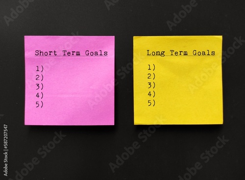 Pink and yellow note stick on wall with lists of SHORT TERM GOALS and LONG TERM GOALS, concept of goals setting goals, easy ones to achieve soon and bigger ones to accomplish in the future