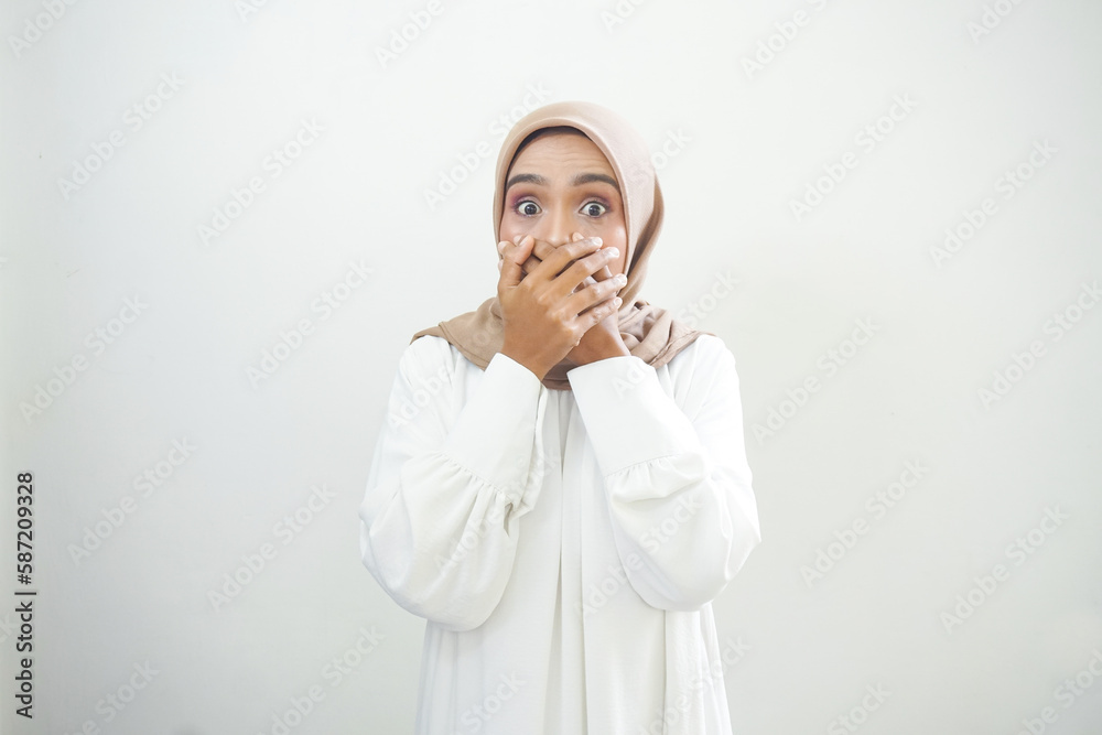 Shocked young Asian Muslim woman dressed in white covering mouth with hand for mistake isolated on white background.
