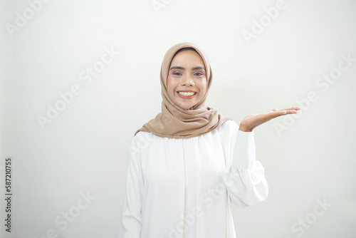 Smiling young Asian muslim woman in wearing casual clothes showing copy space on palm on white background