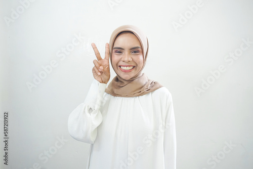 Cheerful young Asian woman in white dress showing peace sign over eyes isolated over white background.