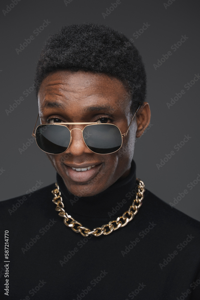 Obraz premium Joyful guy of african ethnic with chain and sunglasses isolated on grey background.