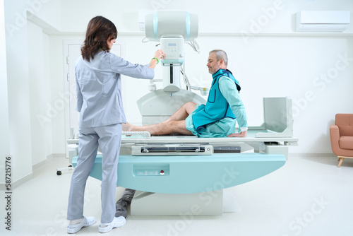 Female doctor preparing machine for medical scan of man knee