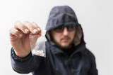 Dangerous man in hooded jacket and sunglasses holding plastic transparent bags with white pills, drug dealer offering narcotics