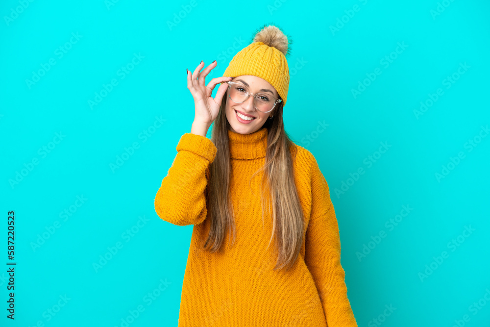 Young caucasian woman wearing winter jacket isolated on blue background with glasses and happy Young caucasian woman wearing winter jacket isolated on blue background with glasses and happy