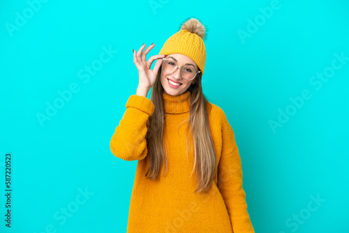 Young caucasian woman wearing winter jacket isolated on blue background with glasses and happy © luismolinero
