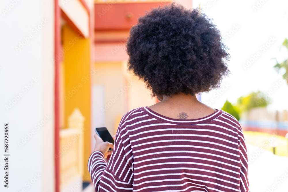 Fototapeta premium African American girl using mobile phone at outdoors in back position