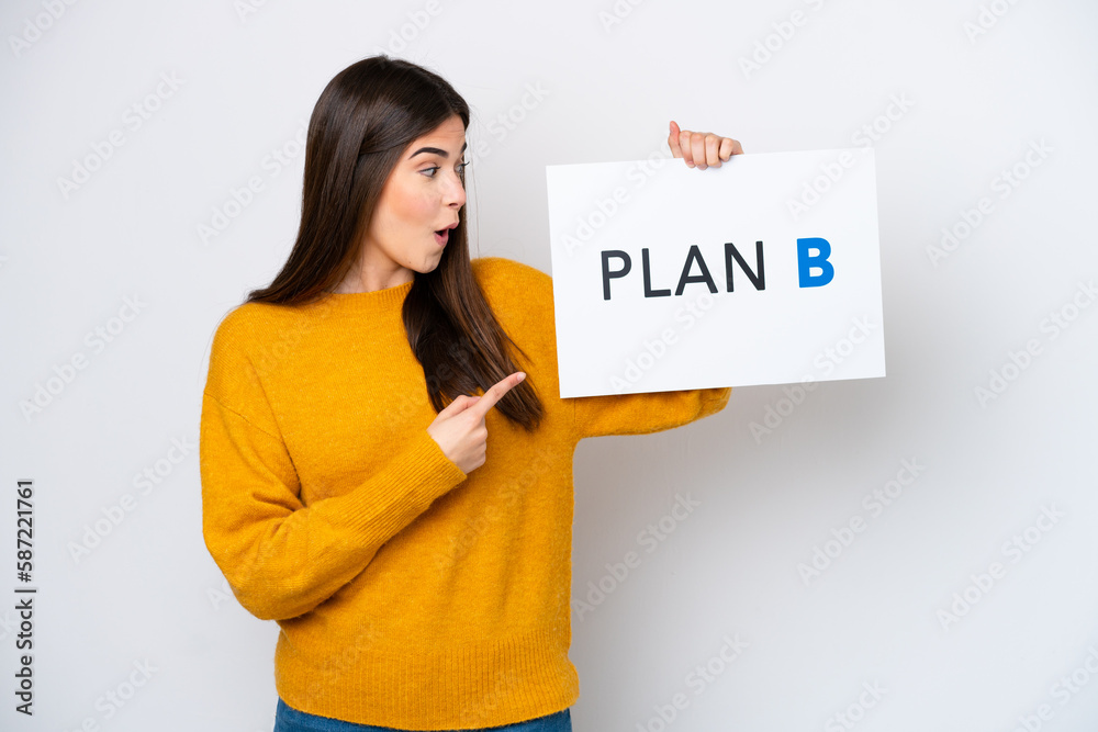 Young Brazilian woman isolated on white background holding a placard with the message PLAN B with surprised expression Young Brazilian woman isolated on white background holding a placard with the message PLAN B with surprised expression
