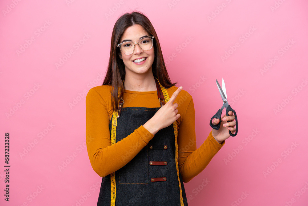 Young Brazilian seamstress woman isolated on pink background pointing to the side to present a product Young Brazilian seamstress woman isolated on pink background pointing to the side to present a product