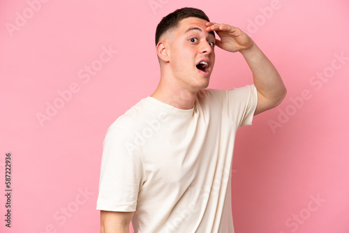 Young Brazilian man isolated on pink background doing surprise gesture while looking to the side