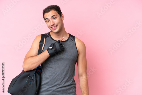Young sport caucasian man with sport bag isolated on pink background pointing to the side to present a product