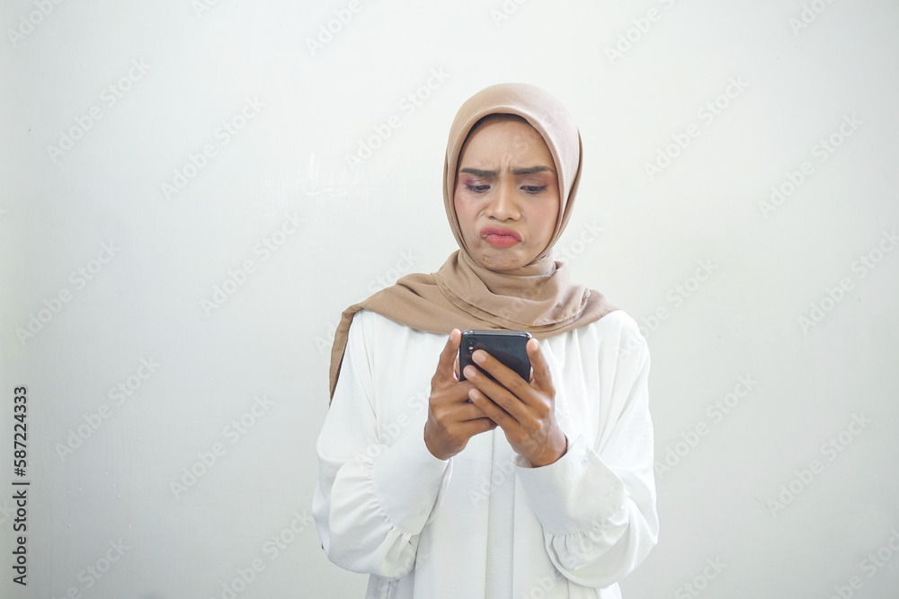 Beautiful smiling Asian Muslim woman wearing hijab Using mobile phone, typing sms message isolated on white background studio portrait. People religious lifestyle concept Beautiful smiling Asian Muslim woman wearing hijab Using mobile phone, typing sms message isolated on white background studio portrait. People religious lifestyle concept