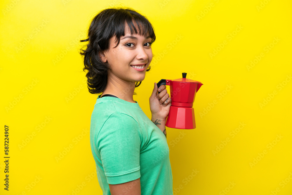 Young Argentinian woman holding coffee pot isolated on yellow background smiling a lot Young Argentinian woman holding coffee pot isolated on yellow background smiling a lot