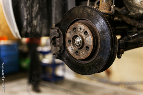 A close-up of the brake caliper on an old car that is lifted on an electric lift in a workshop.