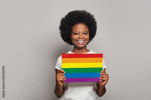 Portrait of african american woman holding LGBT flag on grey background