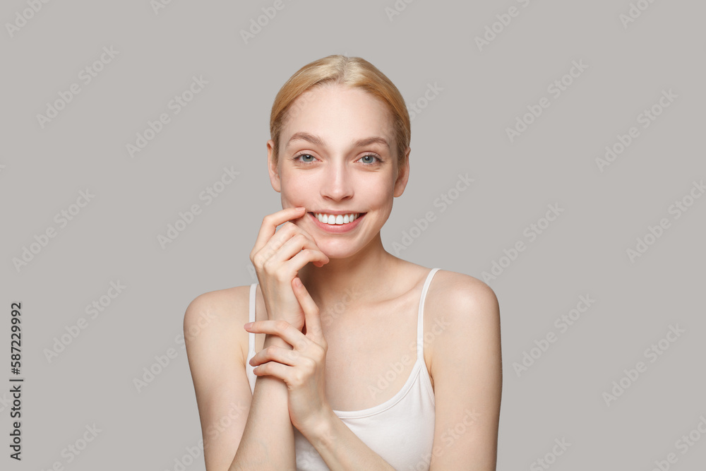 Cheerful attractive woman with clear skin portrait. Female model smiling and holding her hands near her face. Facial treatment, skincare and cosmetology concept