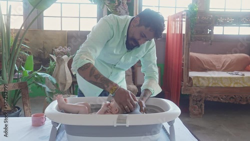 Father washing baby's head in bath thub, ethnic diversity interracial family photo