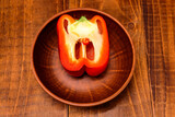One sweet red pepper halved on a clay plate on a wooden table, close up, top view
