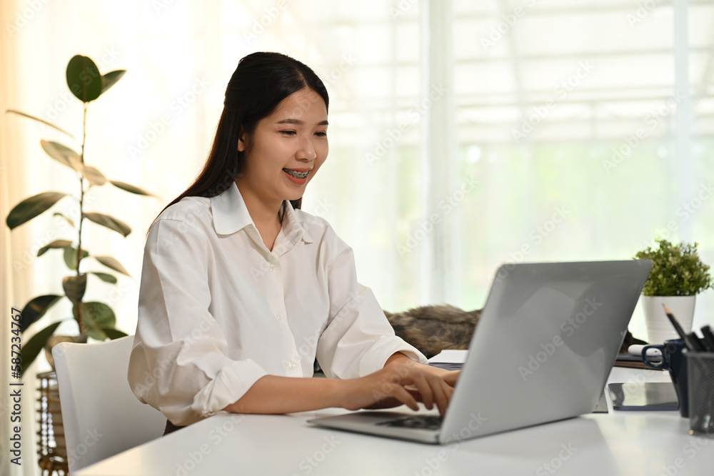 Focused female freelancer in smart casual wears looking at laptop screen, working online or checking email at the morning Focused female freelancer in smart casual wears looking at laptop screen, working online or checking email at the morning