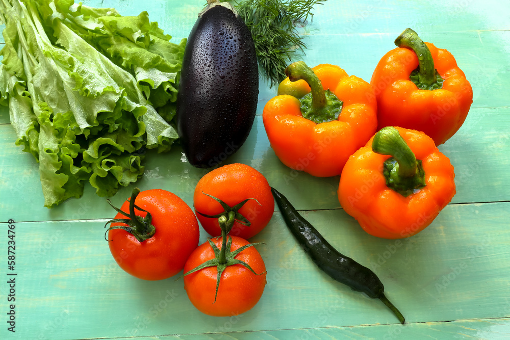 Tomatoes, sweet and bitter peppers, eggplant, dill, lettuce covered with water drops, on a wooden background