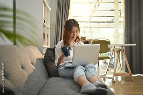 Happy woman relaxing on couch browsing wireless internet or chatting online on laptop computer © Prathankarnpap