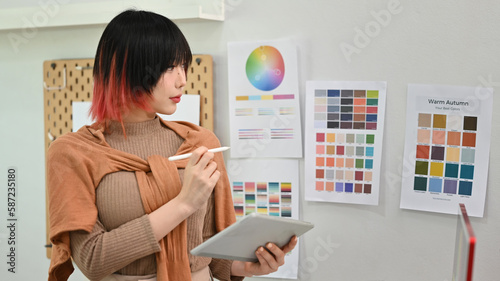 Young asian woman designer illustrator standing in modern design studio and using digital tablet photo