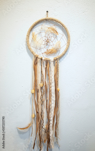 creativity, a dream catcher from threads, feathers hangs on a white wall, in the workshop. Master class, diligence, accuracy, hobby, weaving a dream catcher