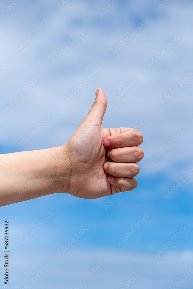 girl making thumbs up gesture on blue sky background.