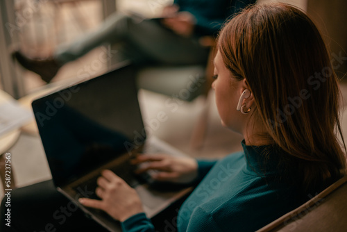 Close up shot of blonde woman listening to music on headphones while working on the lap top