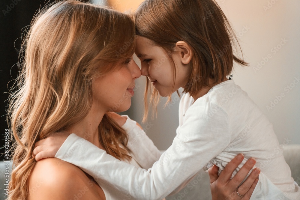 Side view, embracing each other. Mother with her little daughter is together in domestic room Side view, embracing each other. Mother with her little daughter is together in domestic room