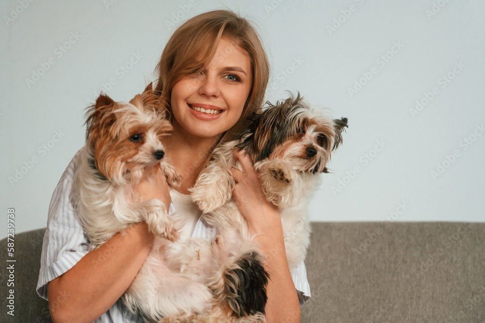 Holding and embracing the animals. Woman is sitting on a sofa with two cute dogs Holding and embracing the animals. Woman is sitting on a sofa with two cute dogs
