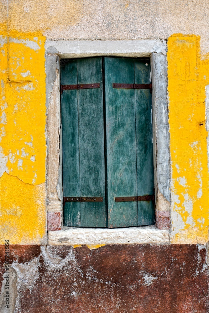 Rustic yellow wall with crumbling paint and a blue window