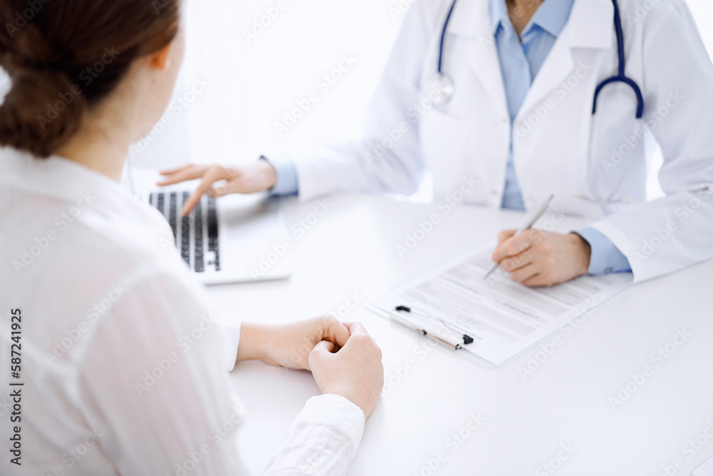 Doctor and patient discussing something and using laptop while sitting opposite each other at the desk in clinic office. Perfect medical service and medicine concept Doctor and patient discussing something and using laptop while sitting opposite each other at the desk in clinic office. Perfect medical service and medicine concept