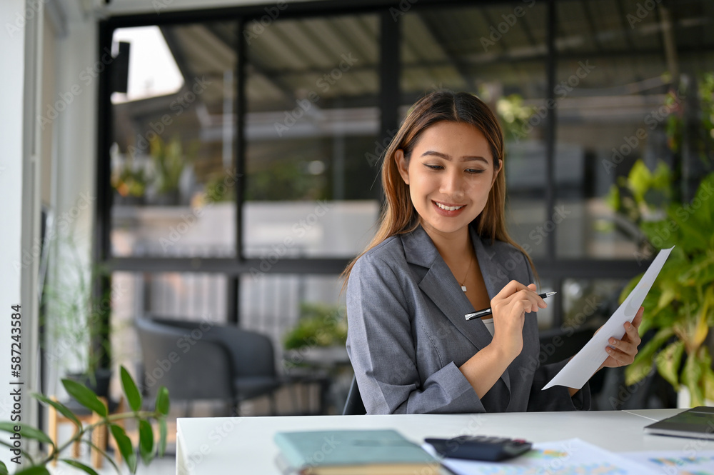 Obraz premium Attractive Asian businesswoman analyzing financial data on reports and working at her desk.