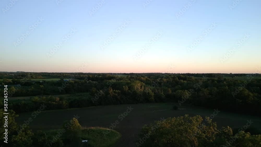 Drone view of a countryside with green forests and fields under blue sky at sunset
