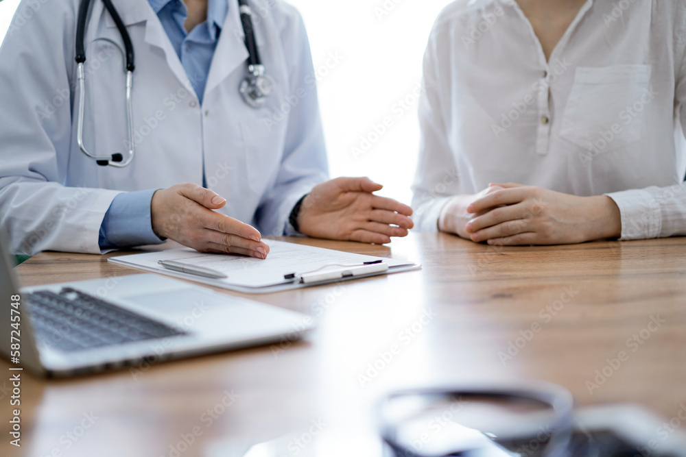 Doctor and patient discussing something while sitting near each other at the wooden desk in clinic, close up of hands. Medicine concept Doctor and patient discussing something while sitting near each other at the wooden desk in clinic, close up of hands. Medicine concept