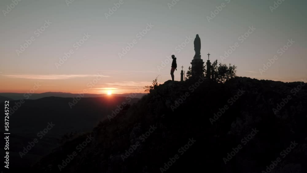 Man reaching the top of a hill with religious figures against a sunset sky Man reaching the top of a hill with religious figures against a sunset sky