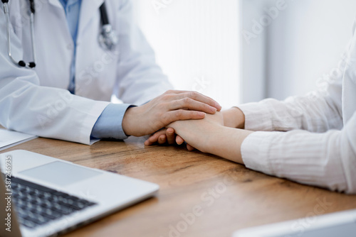 Doctor and patient sitting at the wooden table in clinic. Female physician's hands reassuring woman. Medicine concept