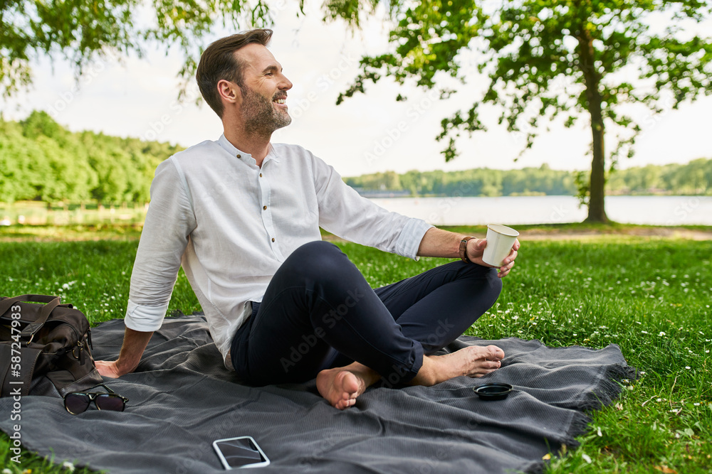 Adult man enjoying spring day in park sitting on blanket with cup of coffee smiling Adult man enjoying spring day in park sitting on blanket with cup of coffee smiling