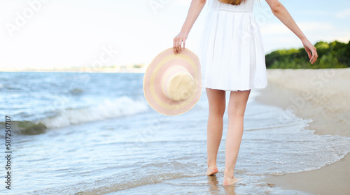 Young woman on a beach holding a white hat. Legs close up